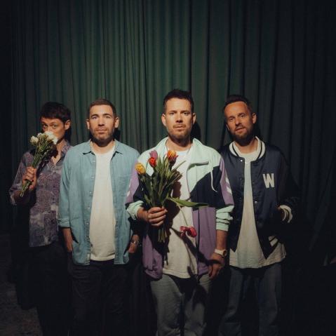Band Revolverheld bei einem Fotoshooting. Die Mitglieder stehen nebeneinander aufgereiht, während der Frontmann einen Blumenstrauß hält.