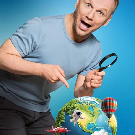 Das Bild zeigt Ralf Schmitz, der mit dem Zeigefinger auf einen grafischen Globus zeigt, während er mit der anderen Hand eine Lupe hält.